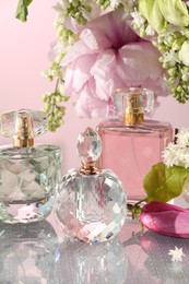 Photo of Luxury perfumes and floral decor on mirror surface against pink background