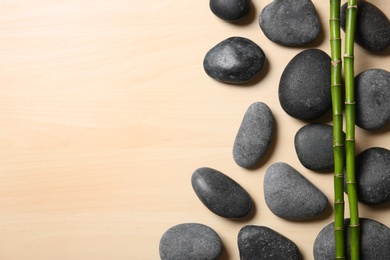 Photo of Spa stones with bamboo stems on wooden background, top view. Space for text