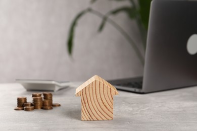 House model, stacked coins, laptop and calculator on grey table, selective focus