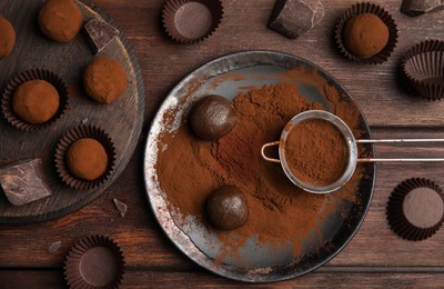 Photo of Delicious chocolate truffles powdered with cocoa on wooden table, flat lay