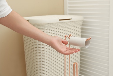 Woman reaching holder with empty toilet paper roll in bathroom, closeup