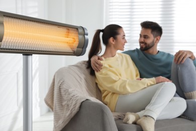 Electric heater and young couple on sofa indoors