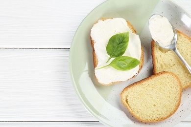 Photo of Pieces of bread with cream cheese and basil leaves on white wooden table, top view. Space for text