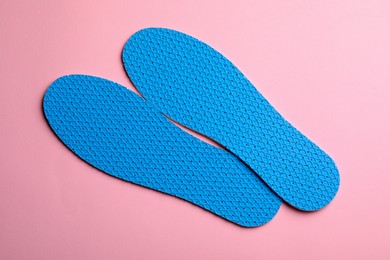 Pair of light blue breathable shoe insoles on pink background, view from above