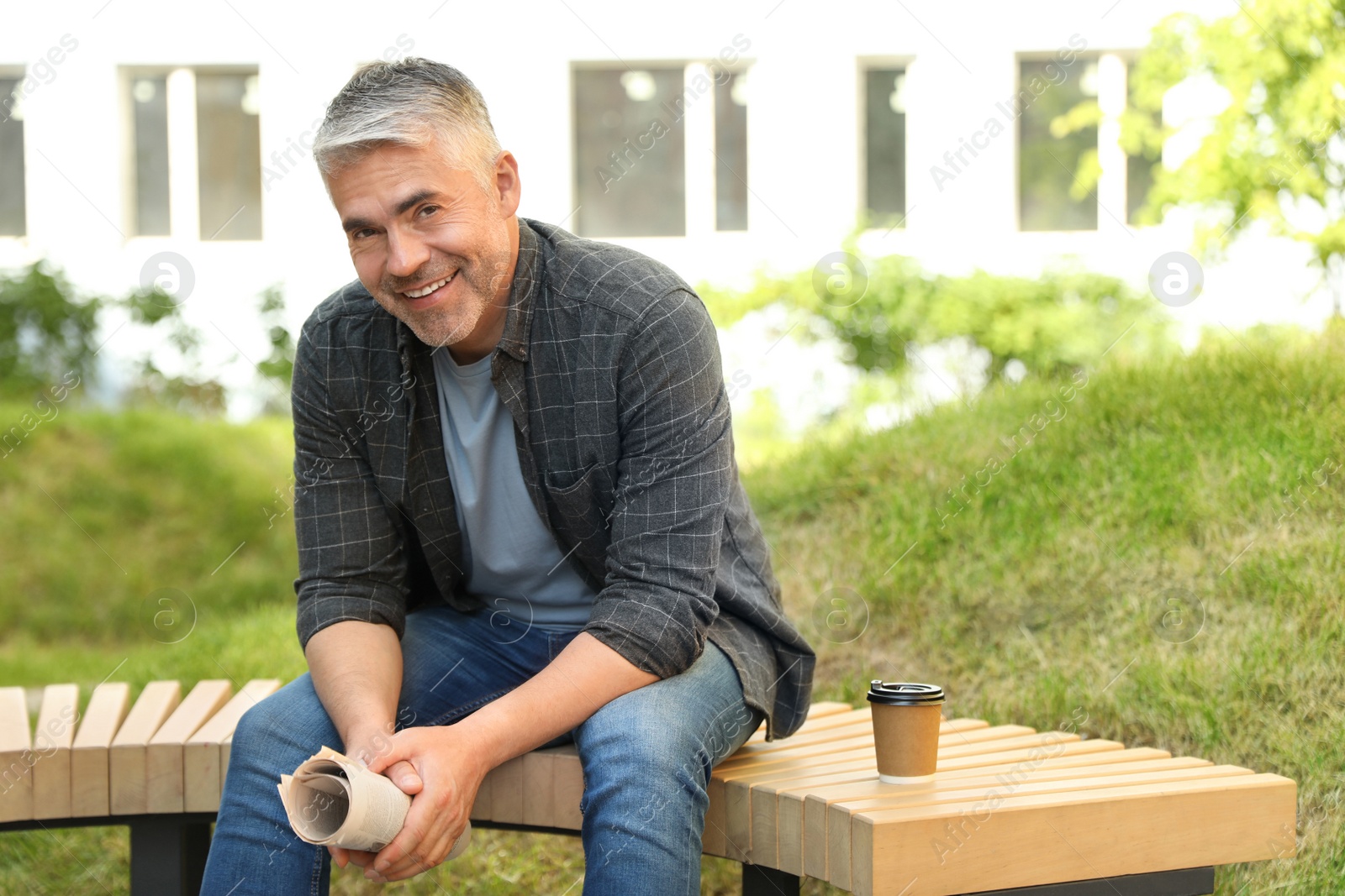 Photo of Handsome mature man with newspaper on bench in park. Space for text