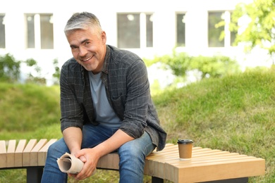 Handsome mature man with newspaper on bench in park. Space for text