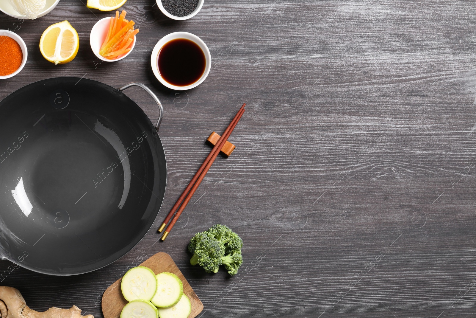 Photo of Empty iron wok, chopsticks and ingredients on grey wooden table, flat lay. Space for text