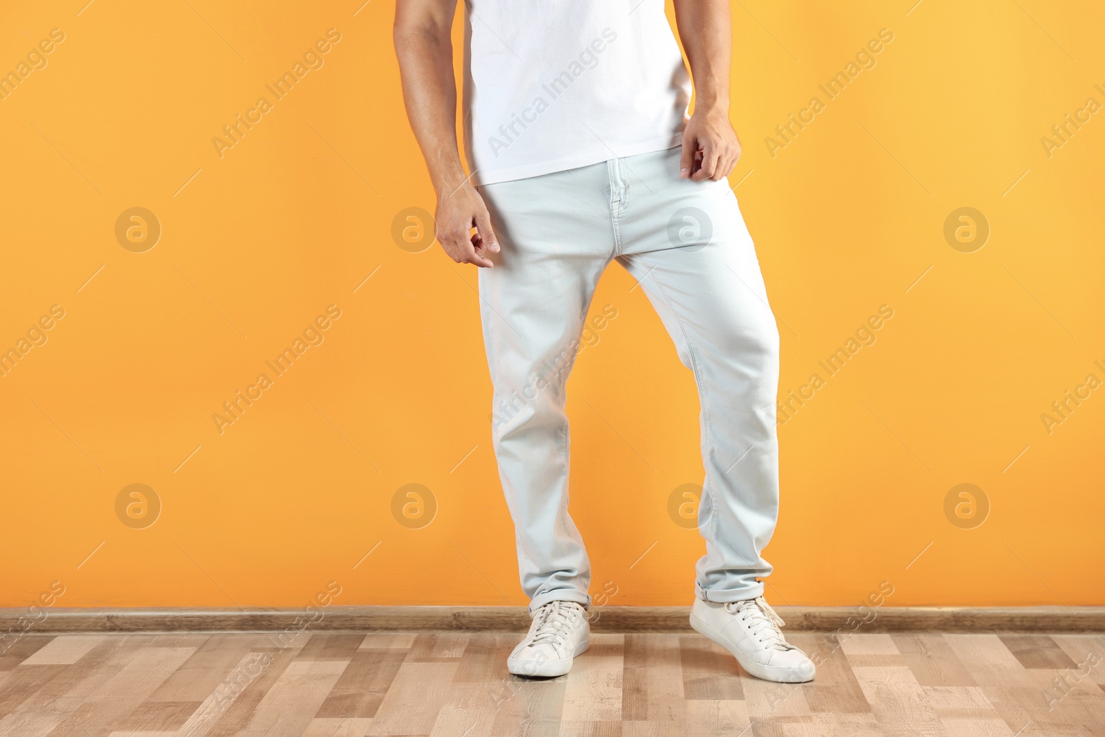 Photo of Young man in stylish jeans near color wall, focus on legs