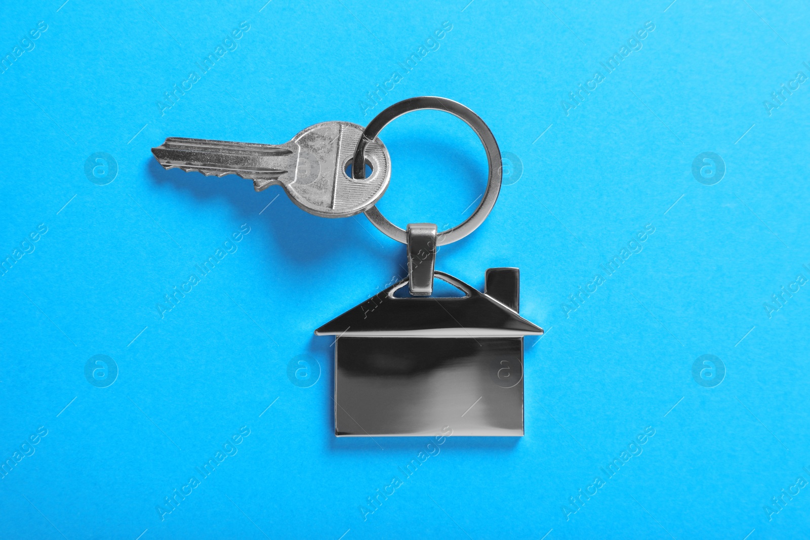 Photo of Key with trinket in shape of house on blue background, top view. Real estate agent services