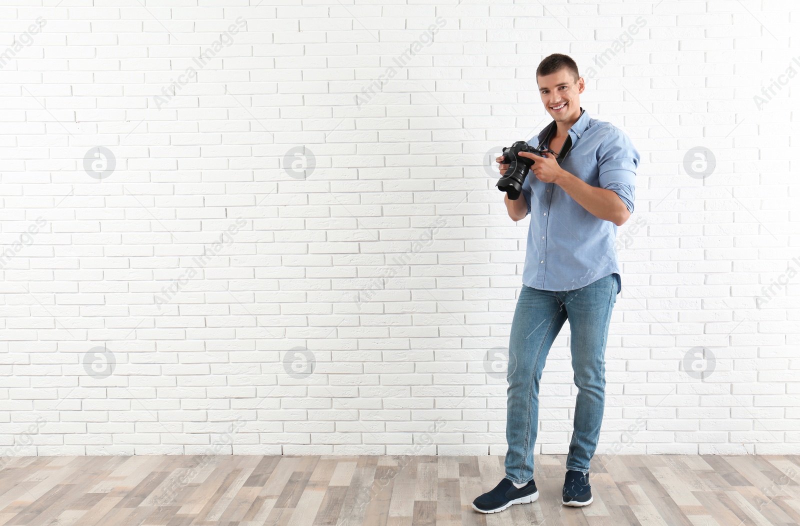 Photo of Young photographer with professional camera near brick wall. Space for text