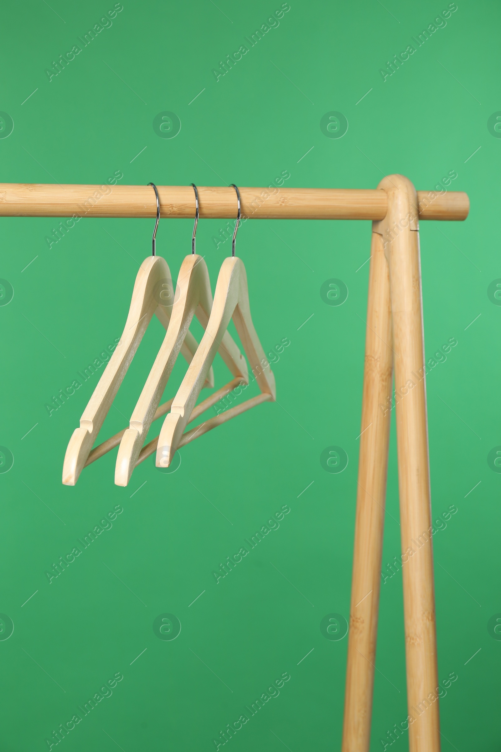 Photo of Empty clothes hangers on wooden rack against green background