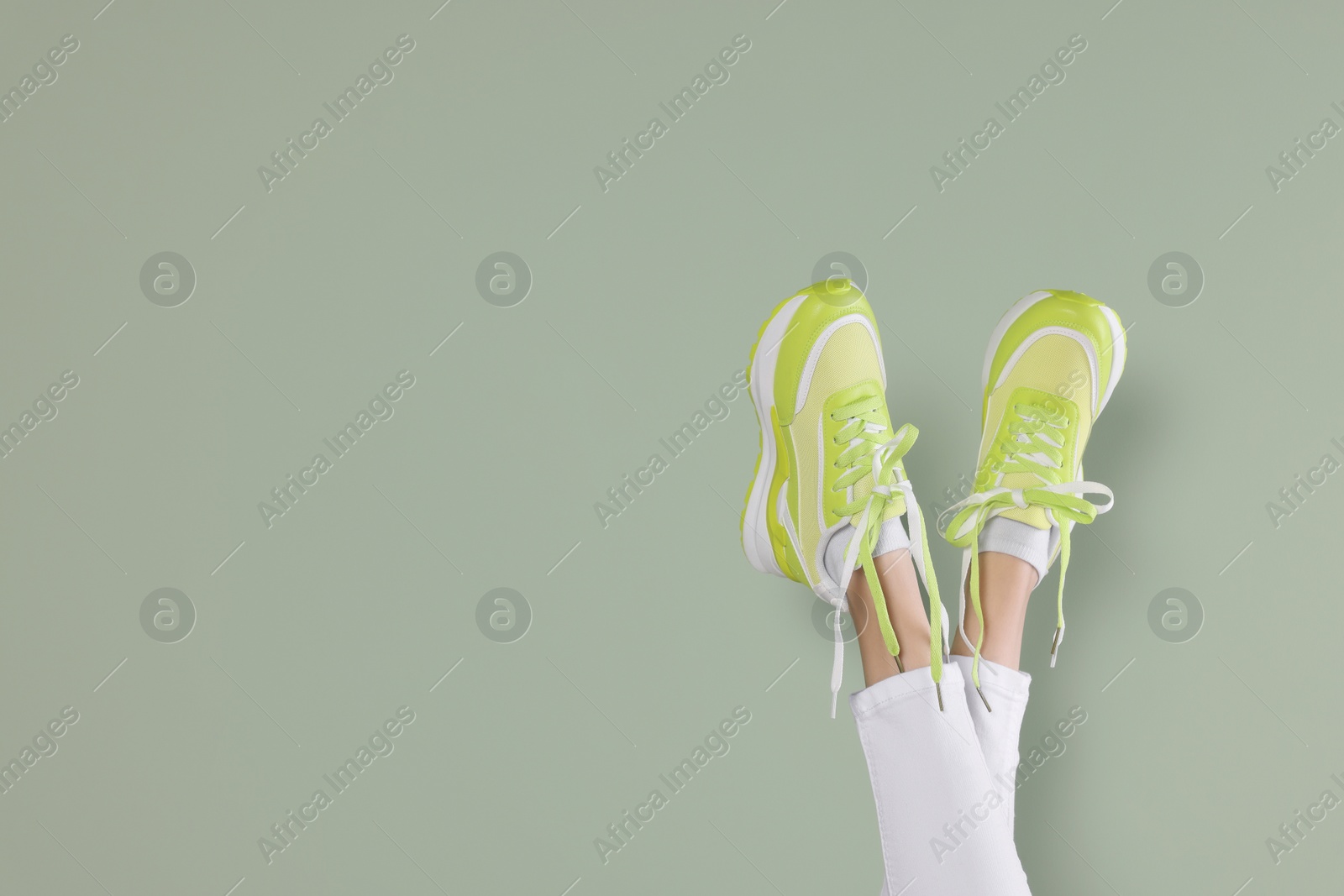 Photo of Woman wearing pair of new stylish sneakers near light green background, closeup. Space for text