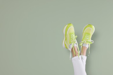Photo of Woman wearing pairnew stylish sneakers near light green background, closeup. Space for text