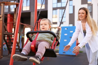 Photo of Happy nanny and cute little boy on swing outdoors