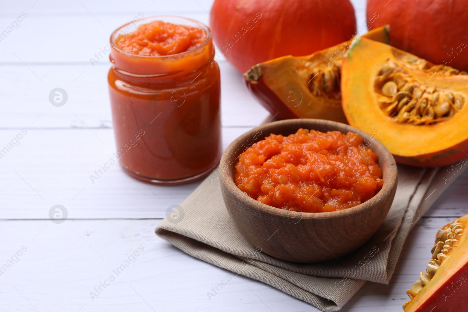 Photo of Delicious pumpkin jam and fresh pumpkins on white wooden table