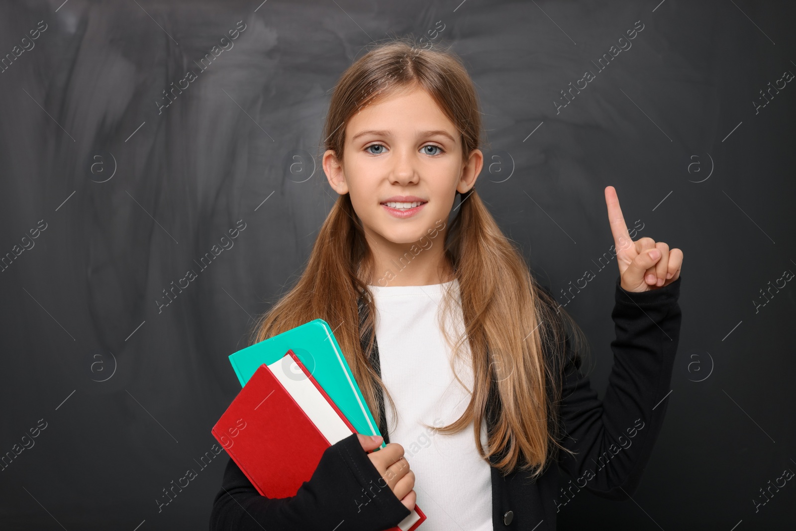 Photo of Smiling schoolgirl pointing at something near blackboard