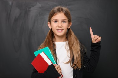 Photo of Smiling schoolgirl pointing at something near blackboard