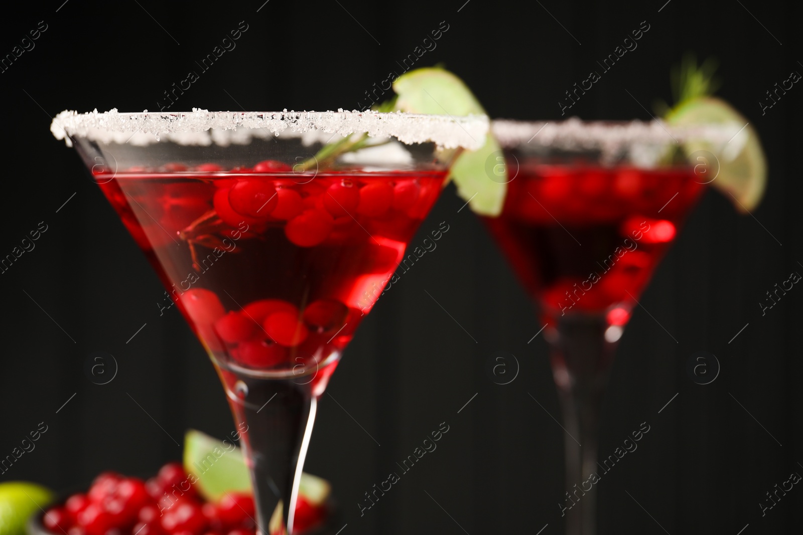 Photo of Tasty cranberry cocktail with rosemary and lime in glasses against black background, closeup