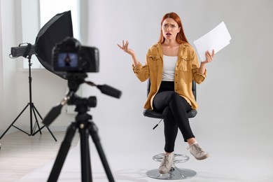 Photo of Casting call. Emotional woman with script performing in front of camera against light grey background at studio