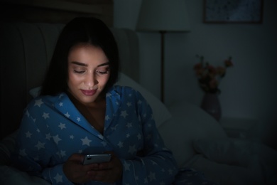 Photo of Happy woman using mobile phone in dark bedroom