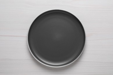 Photo of New dark plate on white wooden table, top view