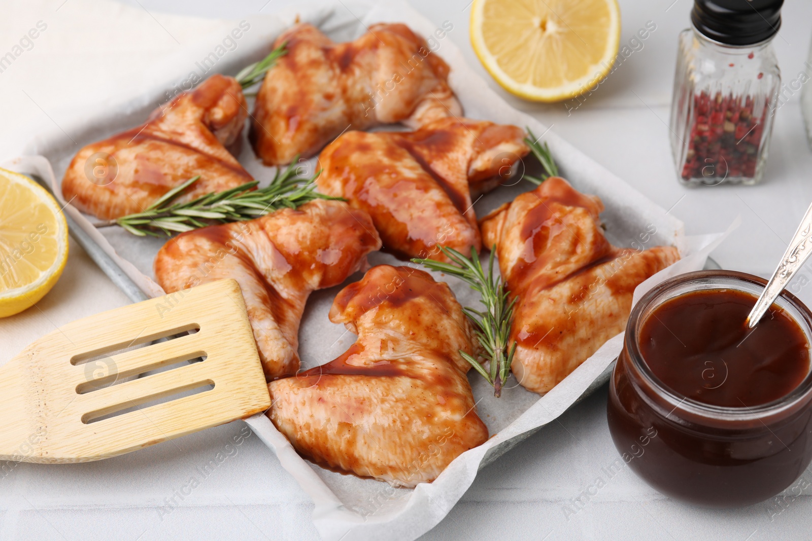 Photo of Raw marinated chicken wings, rosemary and spatula on light tiled table, closeup