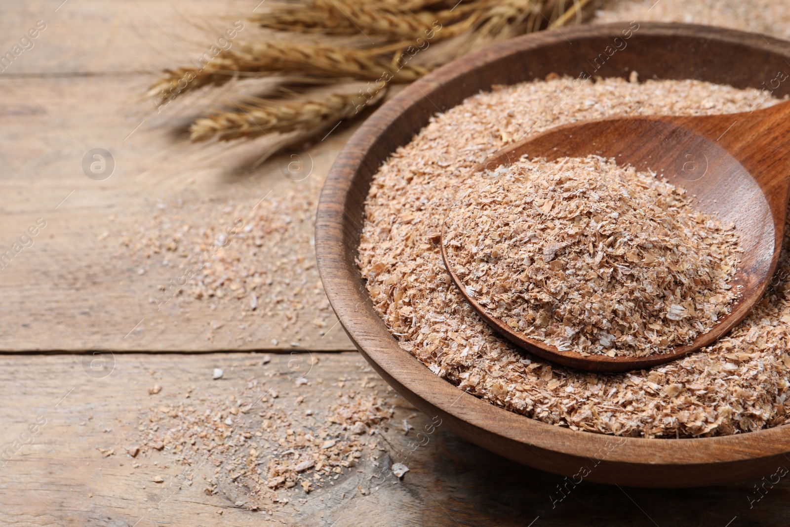 Photo of Wheat bran and spoon in bowl on wooden table, space for text