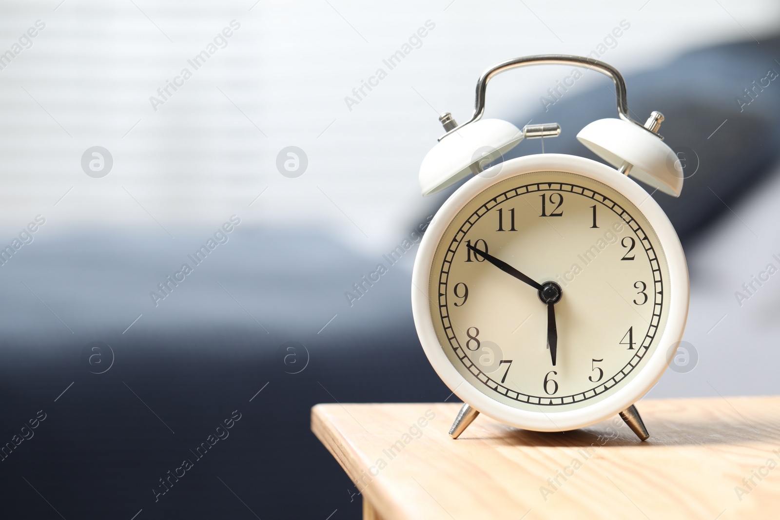 Photo of White alarm clock on wooden nightstand in bedroom, space for text