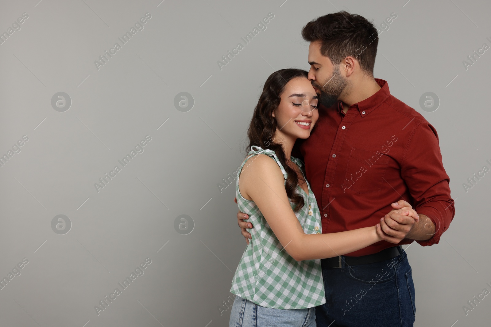 Photo of Man kissing his smiling girlfriend on grey background. Space for text