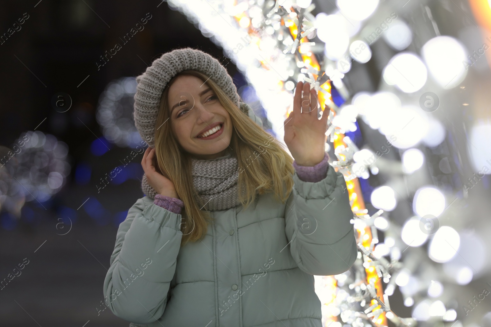 Photo of Happy young woman near festive lights in evening. Christmas celebration