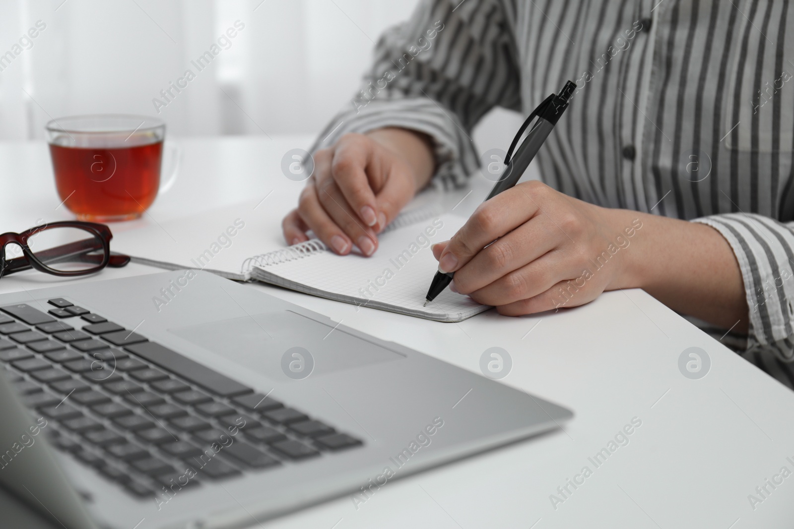 Photo of Left-handed woman writing in notebook at table indoors, closeup