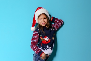 Photo of Cute little girl in Christmas sweater and hat on color background