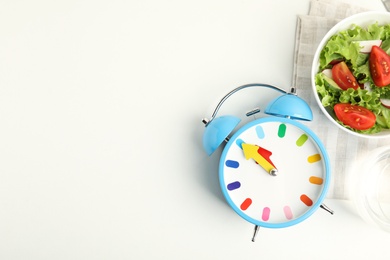 Photo of Alarm clock and salad on white background, top view. Meal timing concept