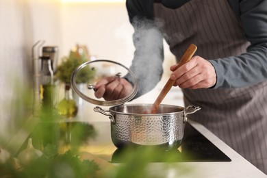 Photo of Man cooking soup on cooktop in kitchen, closeup