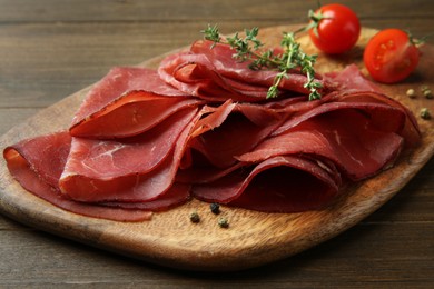 Photo of Tasty bresaola, peppercorns, tomatoes and thyme on wooden table, closeup