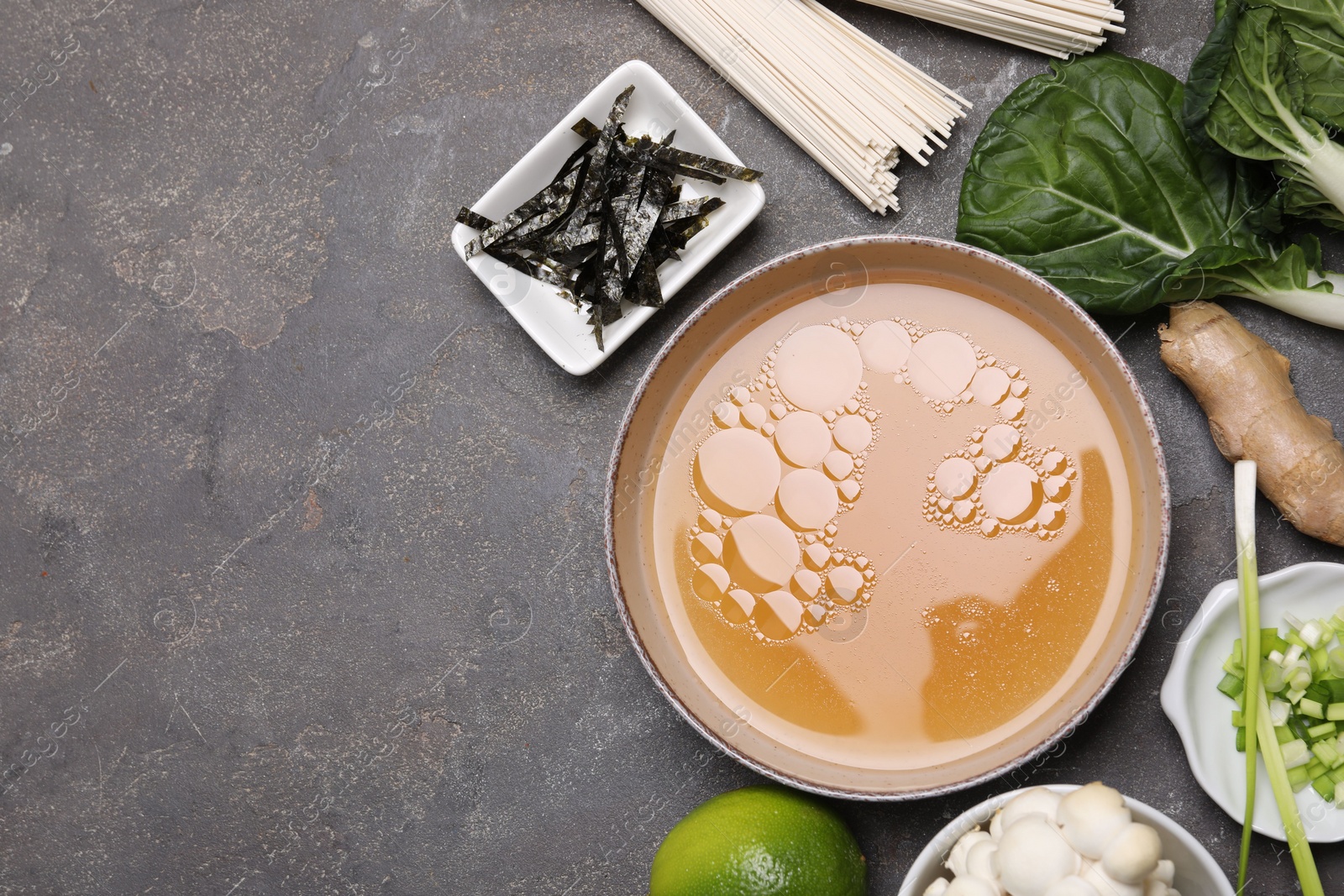 Photo of Cooking delicious ramen soup. Different ingredients on gray table, flat lay. Space for text