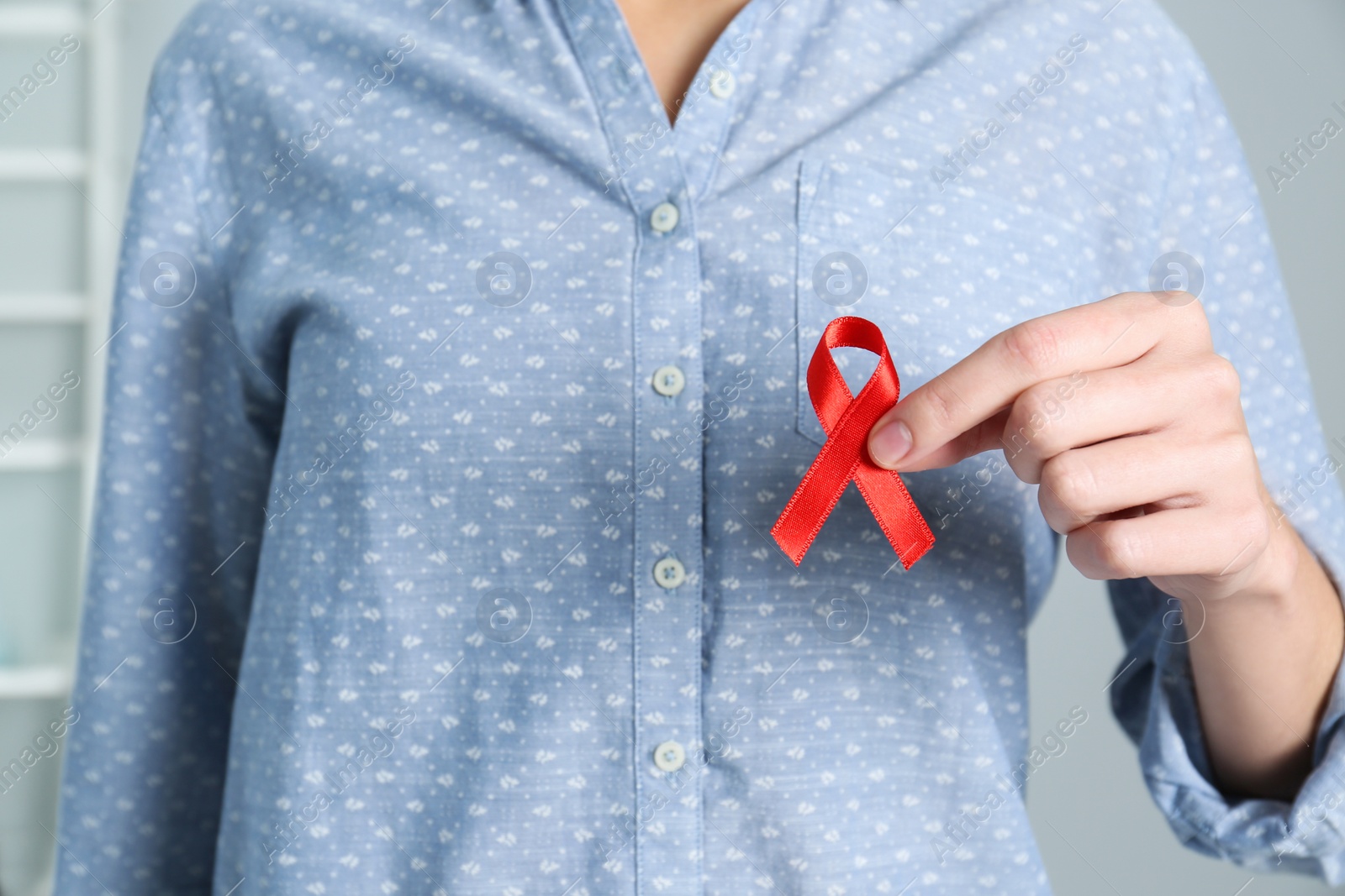 Photo of Woman holding red awareness ribbon indoors, closeup with space for text. World AIDS disease day
