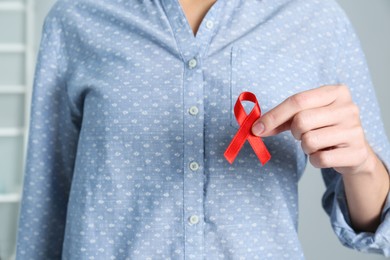 Woman holding red awareness ribbon indoors, closeup with space for text. World AIDS disease day