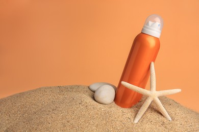 Photo of Sand with bottle of sunscreen, starfish and stones against orange background, space for text. Sun protection