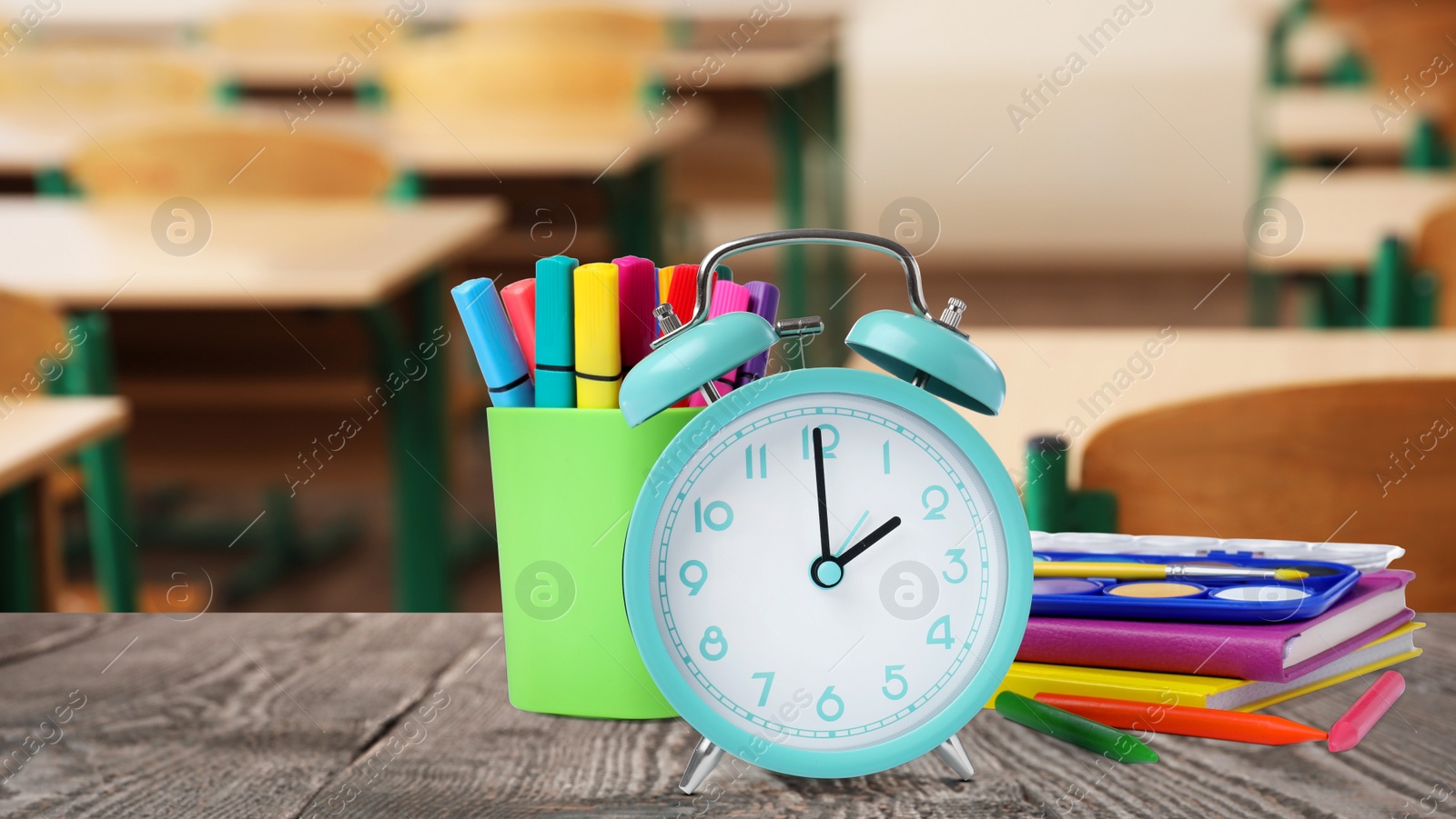 Image of Turquoise alarm clock and different stationery on wooden table in classroom