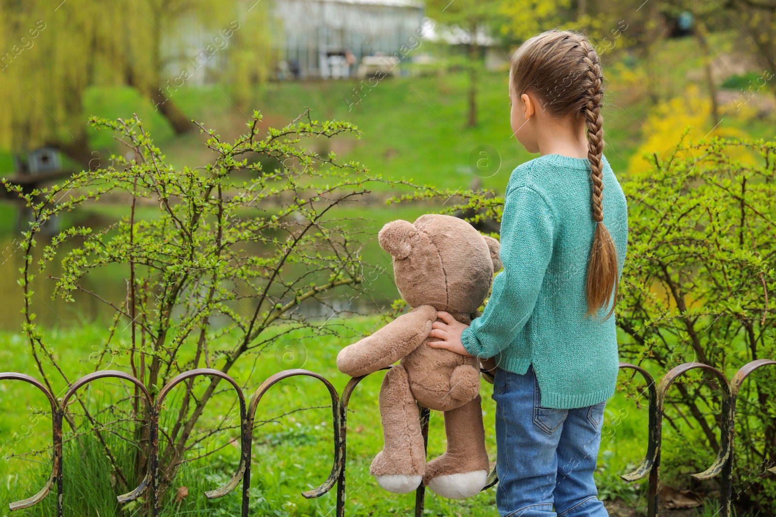 Photo of Little girl with teddy bear outdoors, back view. Space for text