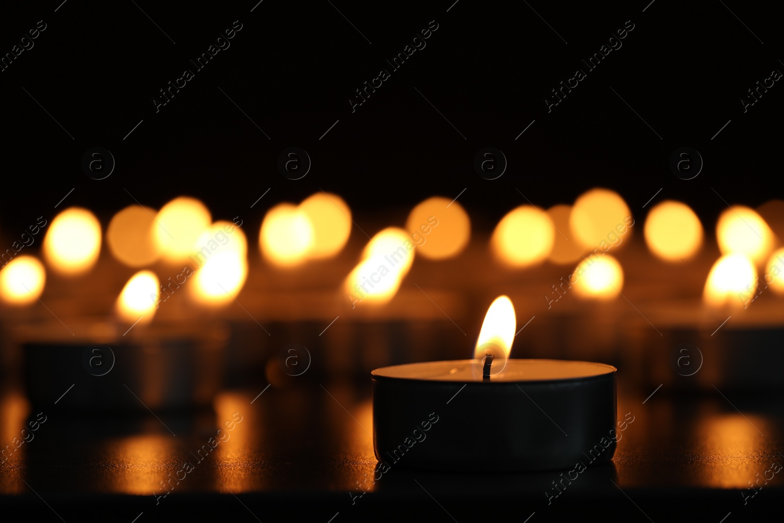 Photo of Burning candles on dark surface against black background, closeup. Space for text