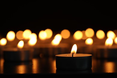Burning candles on dark surface against black background, closeup. Space for text