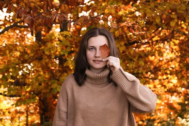 Photo of Portrait of beautiful young woman with autumn leaf in forest