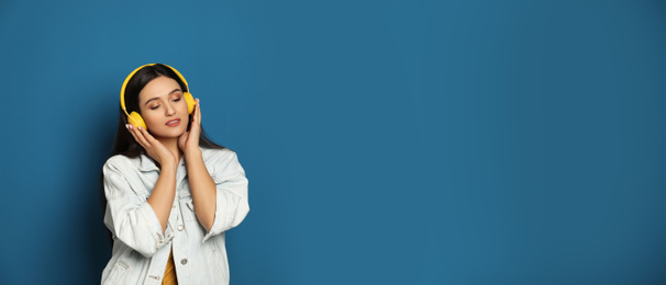 Young woman listening to music with headphones on blue background, space for text. Banner design