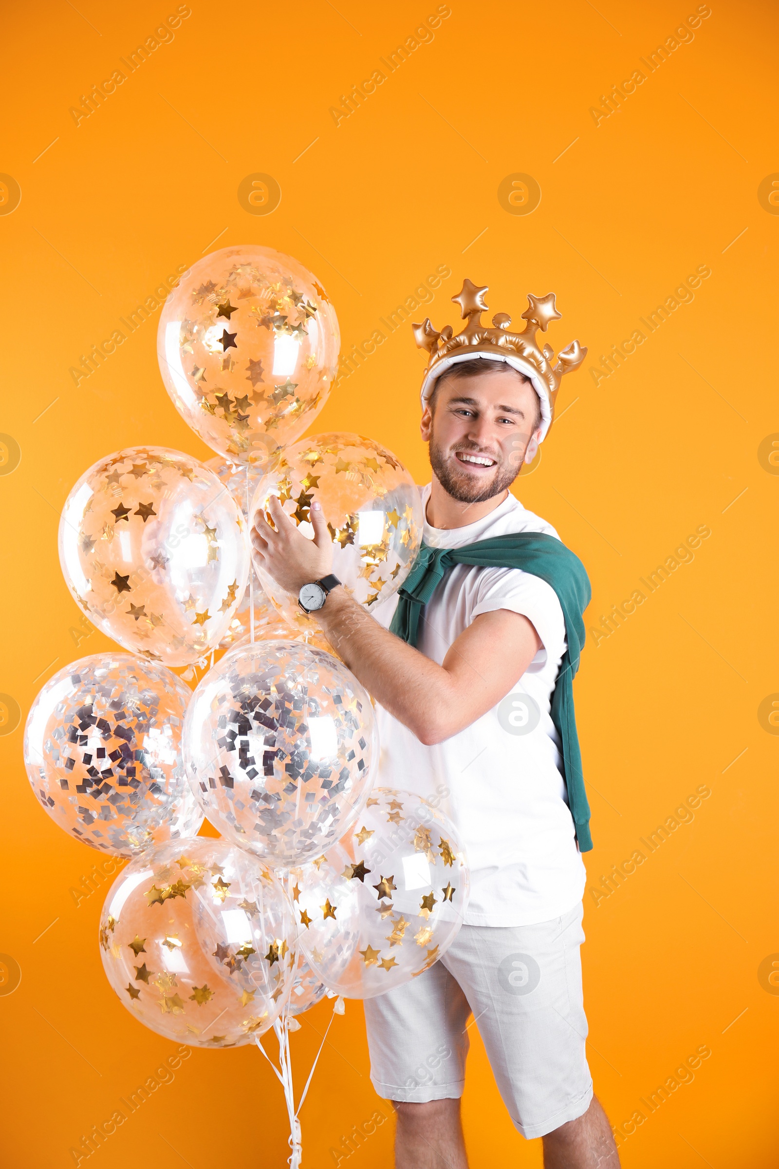 Photo of Young man with crown and air balloons on color background