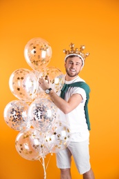 Young man with crown and air balloons on color background
