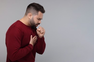 Photo of Sick man coughing on gray background, space for text