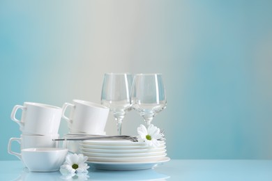 Photo of Set of many clean dishware, cutlery, flowers and glasses on light blue table. Space for text