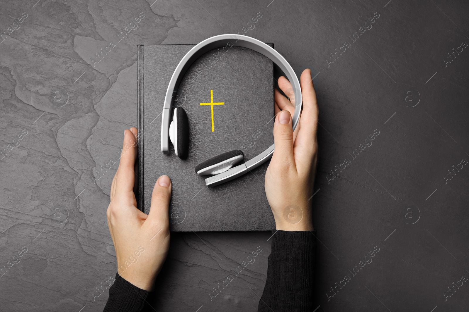 Photo of Woman with Bible and headphones at black table, top view. Religious audiobook